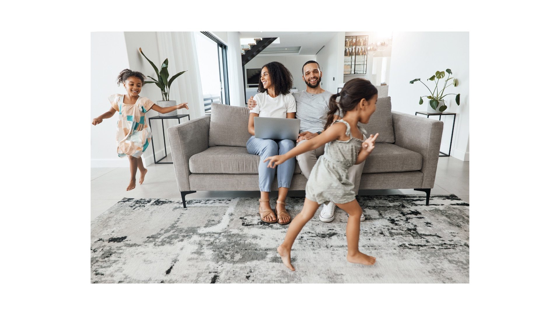 Two adults seated on a sofa while two children play in a bright living room