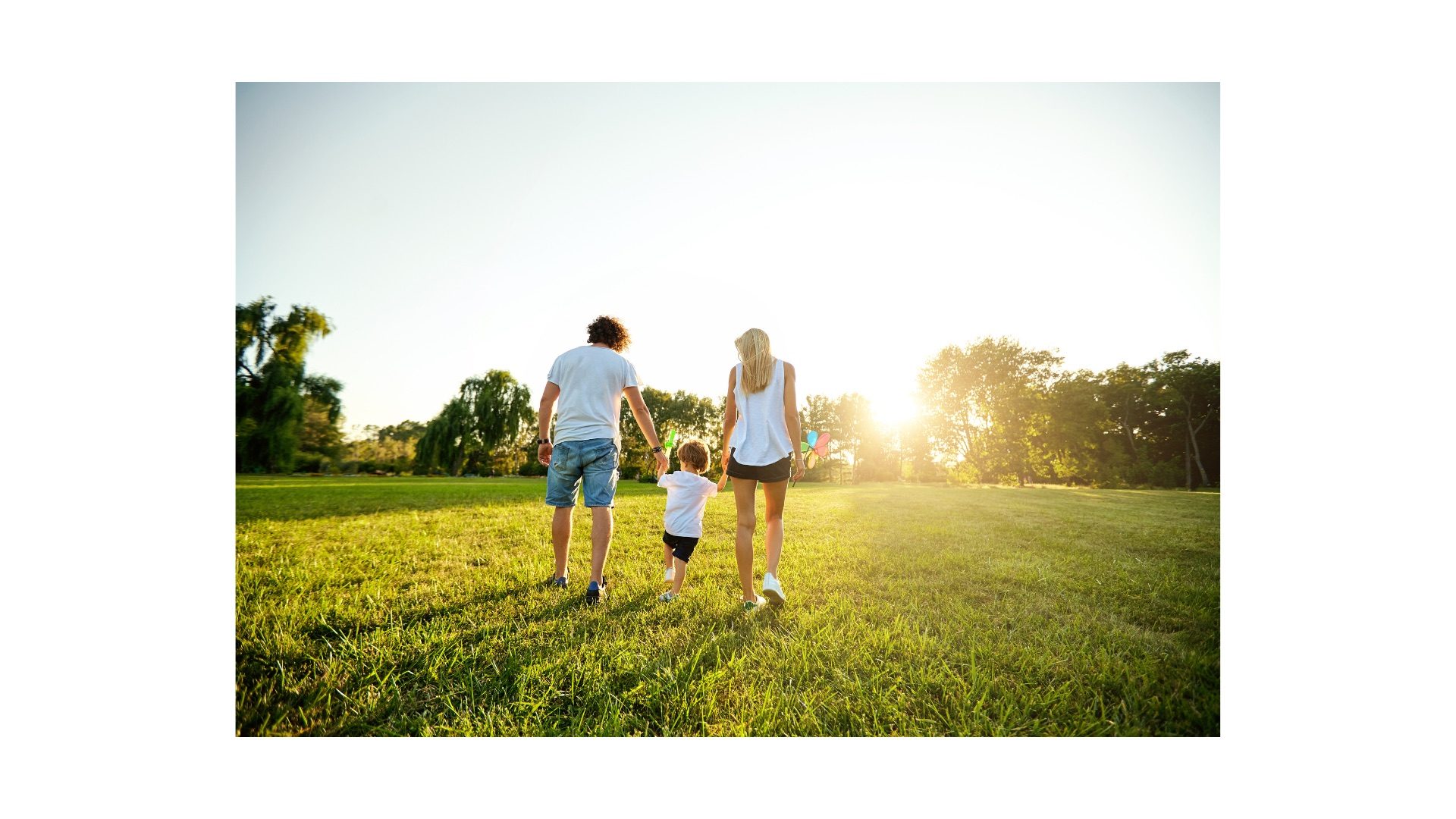 Two adults and a small child walking together through a sunlit park