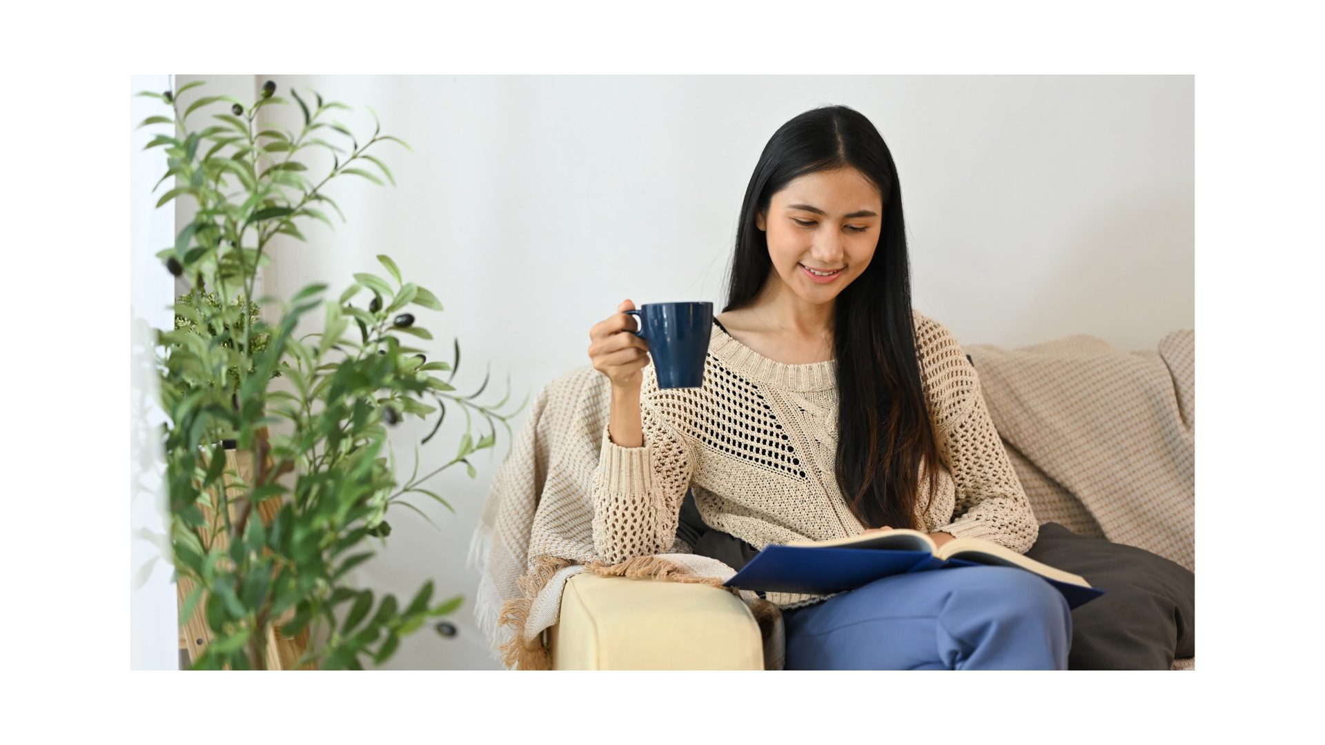 A woman reading on a sofa while holding a mug